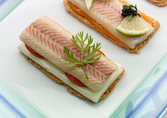 Canapés  de pescado ahumado sobre una base de queso, tomate sobre bandeja de cristal