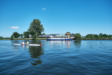 Amersfoort, Hoogland, the Netherlands June 13, 2021, Bicycle boat, ferry eemland on the river Eem with canoeist and a dike and blue sky in the background. Boat trip through the Eemvallei and 't Gooi