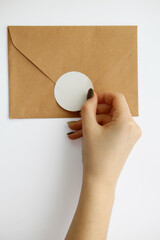 female hand with manicure glues a round sticker on a brown envelope on a white background.  mockup...