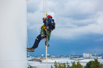 Close-up male workers control equipment rope down tank rope access background cloud storm.