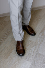 Young man groom in a gray suit is preparing for the wedding. Brown shoes.