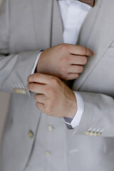 Young man groom in gray suit getting ready for wedding dresses jacket