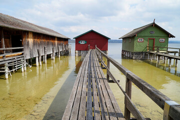 a wooden pier leading to the colorful boat houses on lake Ammersee in the German village Schondorf 