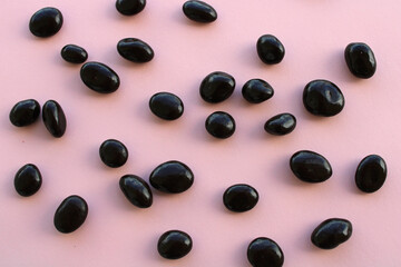 Chocolate drops on pink background, dark chocolate coverd nuts, top view
