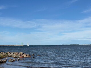 Ein Segelboot l&auml;uft an der Travem&uuml;nder Mole mit dem Leuchtturm vorbei in den Fluss Trave ein. 