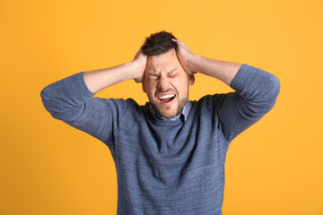 Man suffering from terrible migraine on yellow background