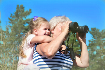 Little girl with her grandmother looking through binoculars outdoor