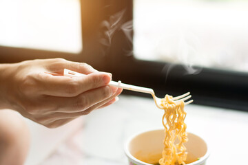 Hand to pickup tasty noodles cup with smoke in bowl selective focus. Asian meal on a table, junk food concept