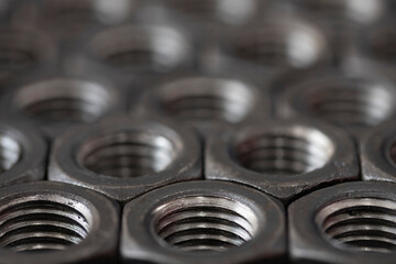 Obraz premium Large threaded steel nuts for bolts stacked in a row close-up. Screw. Abstract background of hexagonal metal nuts for tightening products with space for text.