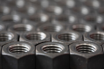 Large threaded steel nuts for bolts stacked in a row close-up. Screw. Abstract background of hexagonal metal nuts for tightening products.