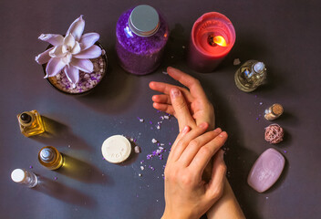 Woman's hands care. Beauty products - cosmetic bottles with essential oil, soap bars, purple sea salt, burning candle on dark blue table top view flatly. Spa treatment, wellness, relaxation. Manicure.