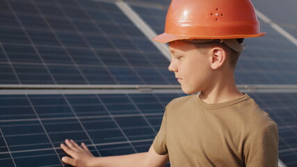 Little boy in a protective helmet at a solar power plant. The concept of children and green...
