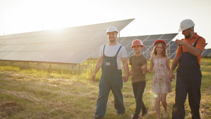 Two parents brought their children to work. Two employees of a solar power plant tell children about the production of electricity. Solar park. Alternative energy concept. Ecological construction