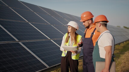 Three employees of alternative power plant walking and talking about scheme of solar panels. Team work. Group of specialists. Camera follows people. Meeting with the investor