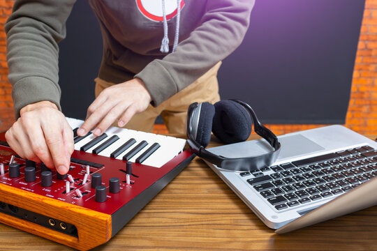 male happy DJ playing red analog synthesizer keyboard with laptop computer and headphone on desk
