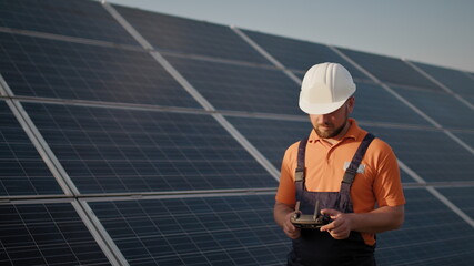 Industrial expert wearing helmet and controlling drone in photovoltaic solar power plant. Solar...