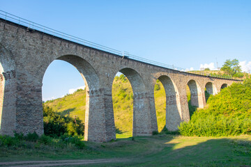 Viaduct in the mountains. Stone railway bridge between the hills on the background of nature, evening lighting.