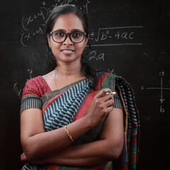 Portrait of Indian ethnic  lady teacher stands in front of a blackboard