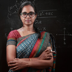 Portrait of Indian ethnic  lady teacher stands in front of a blackboard