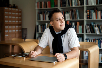 A smart student of the institute is sitting at his desk and looking out the window. Online distance learning in college in the classroom.