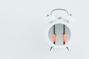 Fototapeta na wymiar Male hands hold prison bars in a white alarm clock isolated on a pastel white background with copy space. Deadline or time limit scene. A creative, abstract idea. Minimalist and surrealist concept.