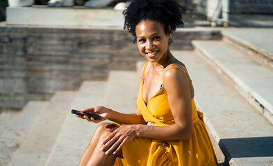 A message on the phone. A freelance African-American woman works outdoors. A female manager in a yellow dress is sitting in a summer cafe in the city.