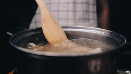 Woman hand stirring boiled soup with pork ribs in a pot on an electric stove in the kitchen. Cooking concept.