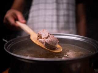 Woman hand stirring boiled soup with pork ribs in a pot on an electric stove in the kitchen. Cooking concept.