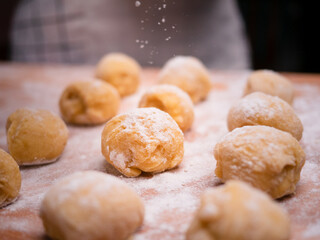 A piece of dough from a whole dough and forms balls for making donuts on a wooden table and sprinkled with flour. Cooking process.
