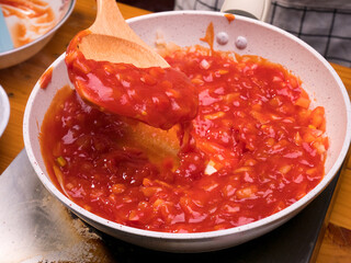 Female hands fries chopped tomatoes and onions making sauce for homemade pizza with healthy ingredients, seasoning with salt and sugar in a saucepan at the kitchen. The process of making pizza.