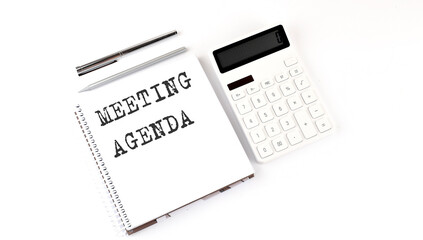 Notepad with text MEETING AGENDA with calculator and pen. White background. Business concept