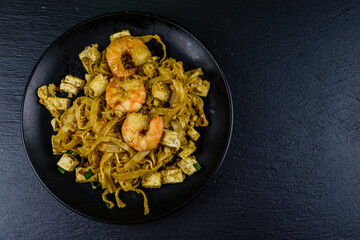 Black plate with pad thai on a slate board. Top view