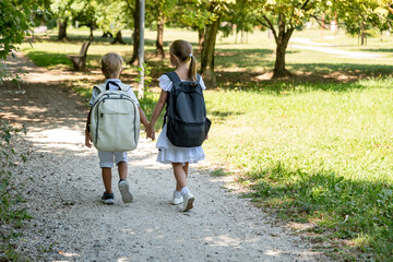 a girl leads her younger brother to school, children in light clothes and with backpacks on their back