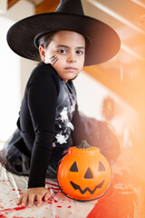 Portrait of caucasian little girl in witch costume next to a pumpkin. Halloween party.