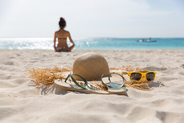 Hat, flip-flops and sunglasses lie on the sand, against the background of the sea and the...