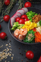 Hawaii shrimp poke with vegetables with ginger, mango, cucumber and avocado, rice, seaweed, tomato. Asian salmon poke on dark stone background.