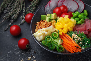 Hawaii tuna poke with vegetables with ginger, mango, cucumber and avocado, rice, seaweed, tomato. Asian salmon poke on dark stone background.