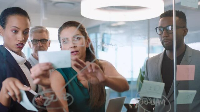 business people using sticky notes brainstorming team leader woman working with colleagues writing on glass whiteboard showing problem solving strategy in office meeting
