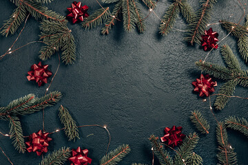 Fototapeta na wymiar Minimal Christmas border with fir branch and red bows on a dark background. Horizontal top composition, flat lay, top view.