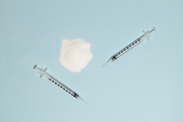 Cocaine or heroin narcotic drug powder and two syringes with a needle on a blue background. Addiction and chemical dependency, illegal drugs concept