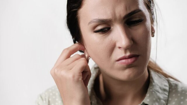 Itching in ear. Puzzled woman on white background with emotions of irritation scratches her ear with finger. Close-up and slow motion