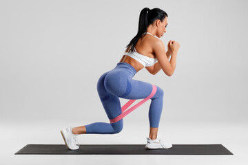 Fitness woman doing exercise for glute with resistance band on gray background. Athletic girl working out