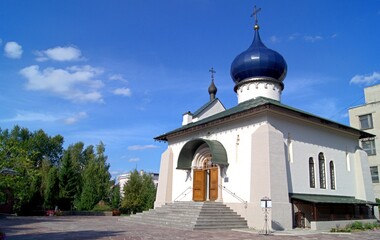 A white Orthodox church building with a blue dome on a clear summer day.