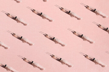 A pattern of a medical syringe on a pink paper background with a shadow, a concept of healthcare,...