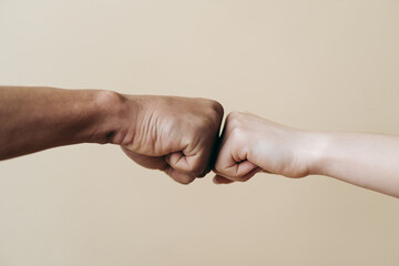 Multiethnic couple hands making fist bump. Young Caucasian woman and African male fists together on beige background. Family Success concept