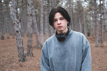 Teenage boy 16-17 year old wear sweatshirt and headphones posing in woods looking at camera. Sad...