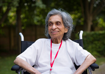 Old woman in a wheelchair smiling in the park in summer UK