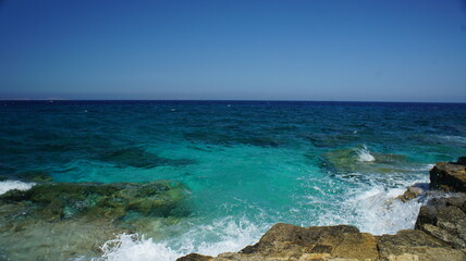 Sea and sky as a wave splash appears on the cliff in the Greek island of koufonisi August 2021