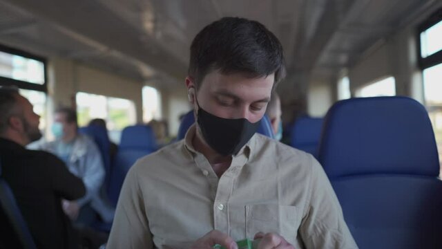 Travel safely on public transport. Young man with face mask using wash hand sanitizer gel dispenser. Passenger with protective mask disinfects hands in train carriage. Masked commuter use alcohol gel.
