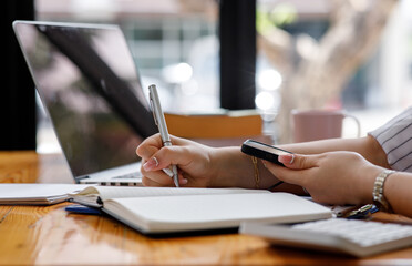 Close up of Casual woman using smartphone, working on laptop computer from home office